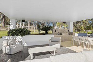 An outdoor patio area with a white ceiling, a stone fireplace, and a seating arrangement including a sofa, chairs, and a table.