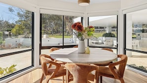 Un comedor moderno con una mesa redonda y seis sillas, ventanas amplias que ofrecen vistas al exterior y una lámpara colgante.