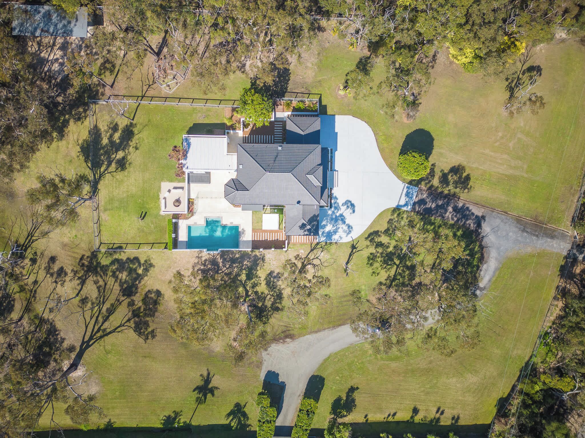 An aerial view of a house with a swimming pool, a patio, and a large yard.