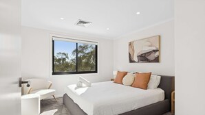 A modern bedroom with a large bed, a chair, a window, and a painting on the wall.