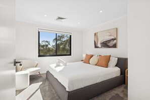 A modern bedroom with a large bed, a chair, a window, and a painting on the wall.
