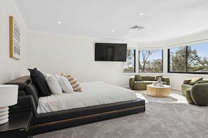 A modern bedroom with a large bed, green armchairs, a round coffee table, and a TV mounted on the wall. - La La Land by Coast Hosting (Kariong)