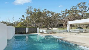 A swimming pool with clear blue water, surrounded by a landscaped garden with various trees and shrubs.