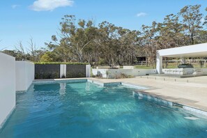 A swimming pool with clear blue water, surrounded by a landscaped garden with various trees and shrubs.