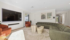 A modern living room with a sectional sofa, a red armchair, and a large flat-screen TV mounted on the wall.