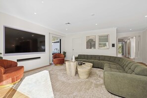 A modern living room with a sectional sofa, a red armchair, and a large flat-screen TV mounted on the wall.