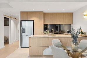Una cucina moderna con mobili in legno, un frigorifero in acciaio inossidabile e un tavolo da pranzo in vetro con sedie.