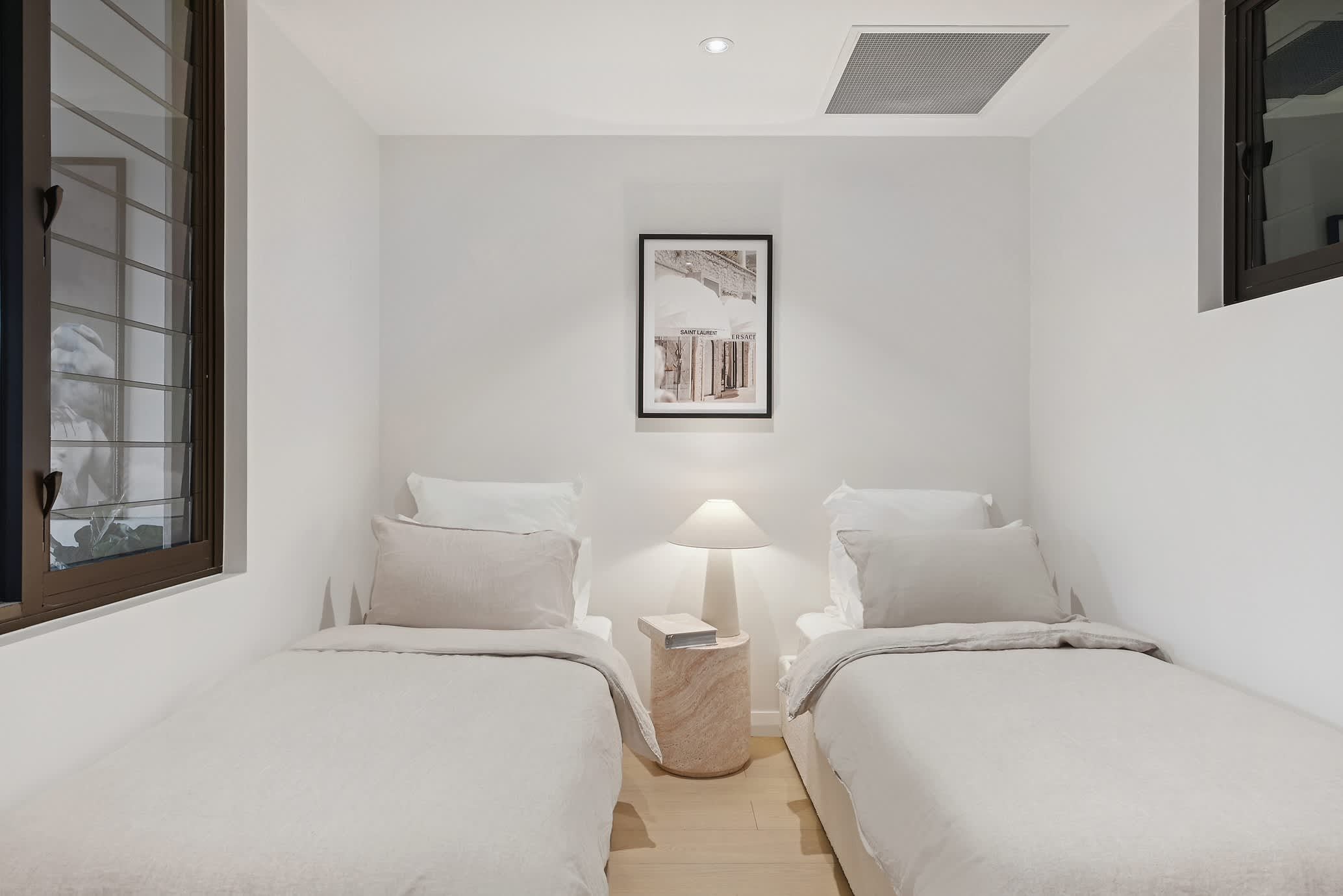 A hotel room with two beds, a nightstand with a lamp, and a framed picture on the wall.