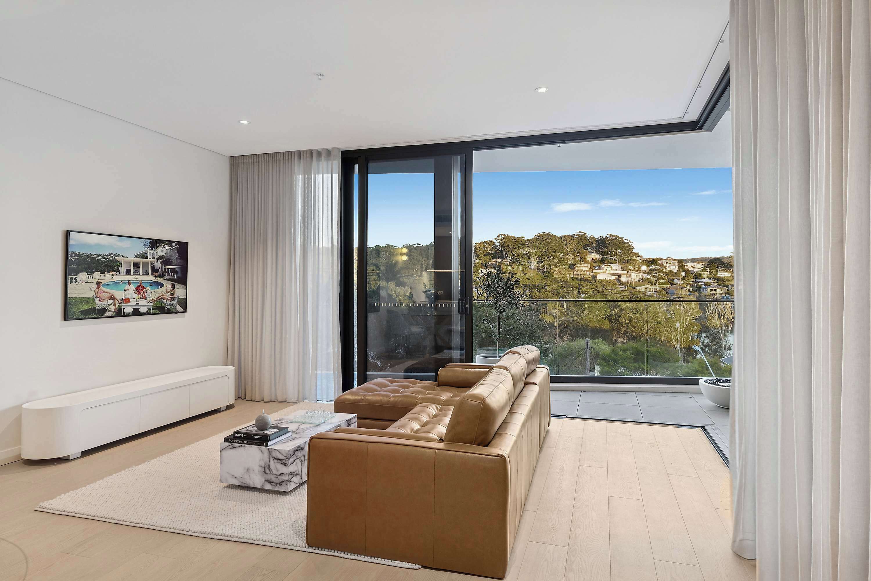 A modern living room with a large window, a sofa, a coffee table, and a painting on the wall.
