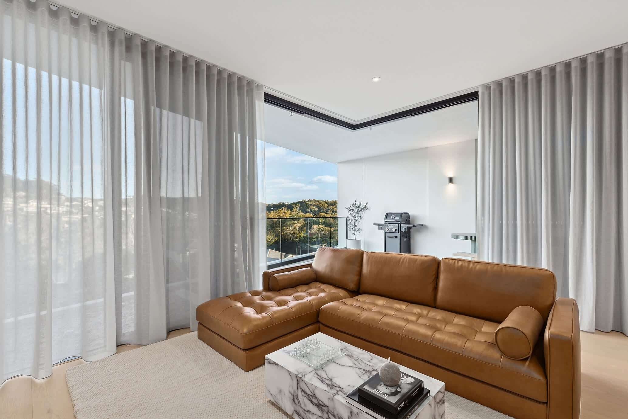 A modern living room with a sectional sofa, a marble coffee table, and sheer curtains.