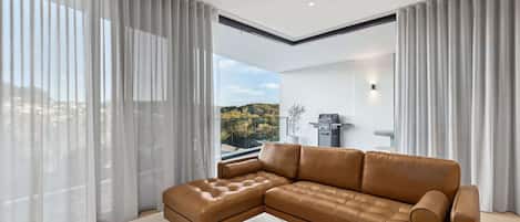 A modern living room with a sectional sofa, a marble coffee table, and sheer curtains.