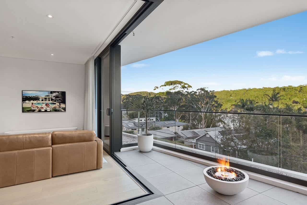 A modern living room with a large window, a beige sofa, a potted plant, and a fireplace.