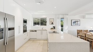 A modern kitchen with white cabinetry, stainless steel appliances, and a large island. - Ocean Views Every Room. 100m to Beach. Sleeps 13 (North Avoca)