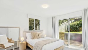 A bedroom with a bed, a chair, a nightstand, and a large window with a view of greenery.