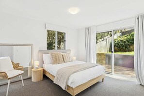 Un dormitorio con cama, silla, mesita de noche y un amplio ventanal con vistas a zonas verdes.
