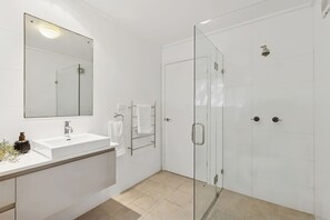 Un baño moderno con ducha de vidrio, lavamanos blanco y espejo grande.
