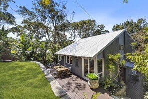 Een huis met een overdekt terras, gazon en diverse planten.