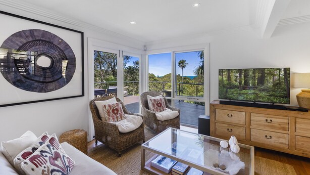 A spacious living room with a large window, wicker furniture, a glass coffee table, and a flat-screen TV.