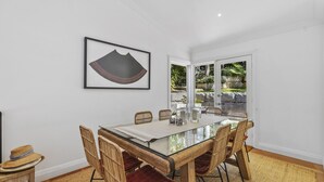 A dining area with a glass-top table, wicker chairs, and a framed artwork on the wall.