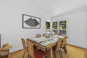 Un comedor con una mesa de vidrio, sillas de mimbre y una obra de arte enmarcada en la pared.