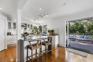 A modern kitchen with a central island, wooden bar stools, and a view of the outdoor deck.