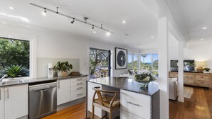 A modern kitchen with a dishwasher, bar stools, and a large window overlooking a garden.