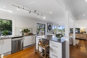Cocina moderna con lavavajillas, taburetes de bar y un amplio ventanal con vistas a un jardín.