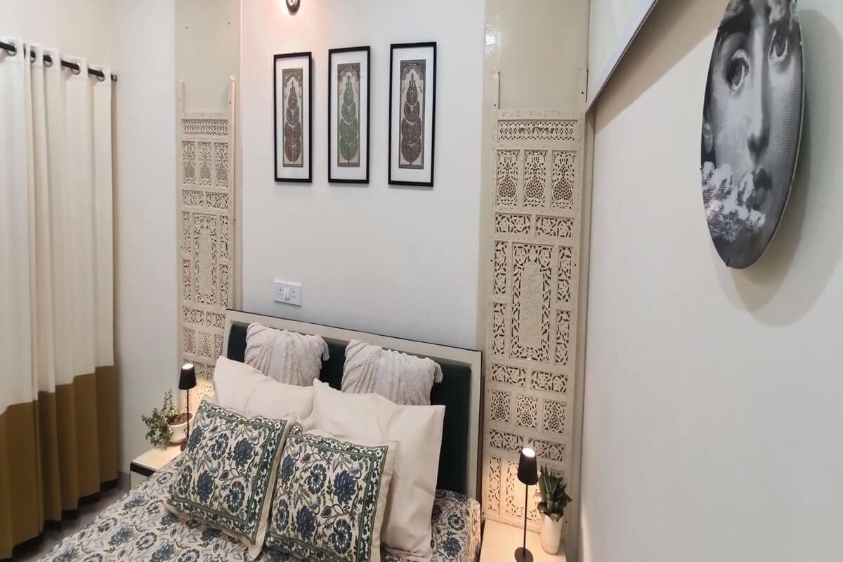 A bedroom with a bed, two wall-mounted lights, a large mirror, and three framed pictures.