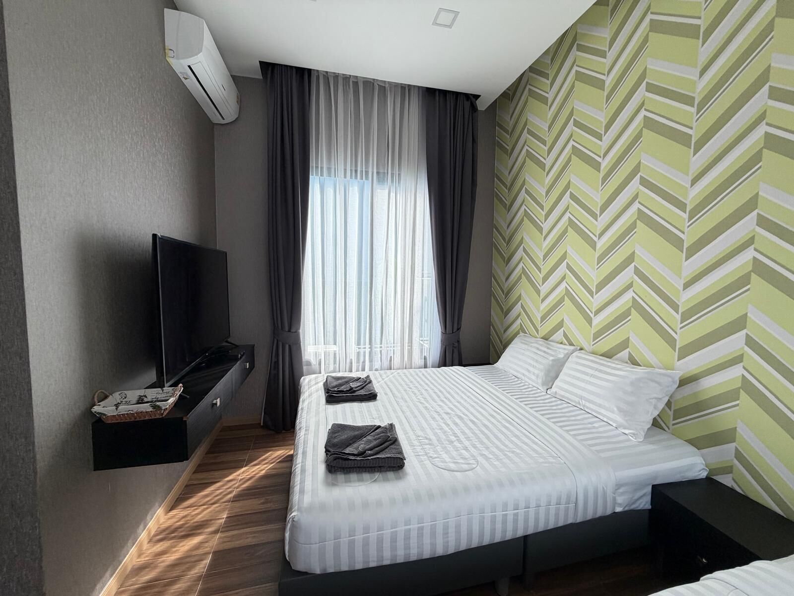 A modern hotel room with a bed, a TV, and a window with curtains.