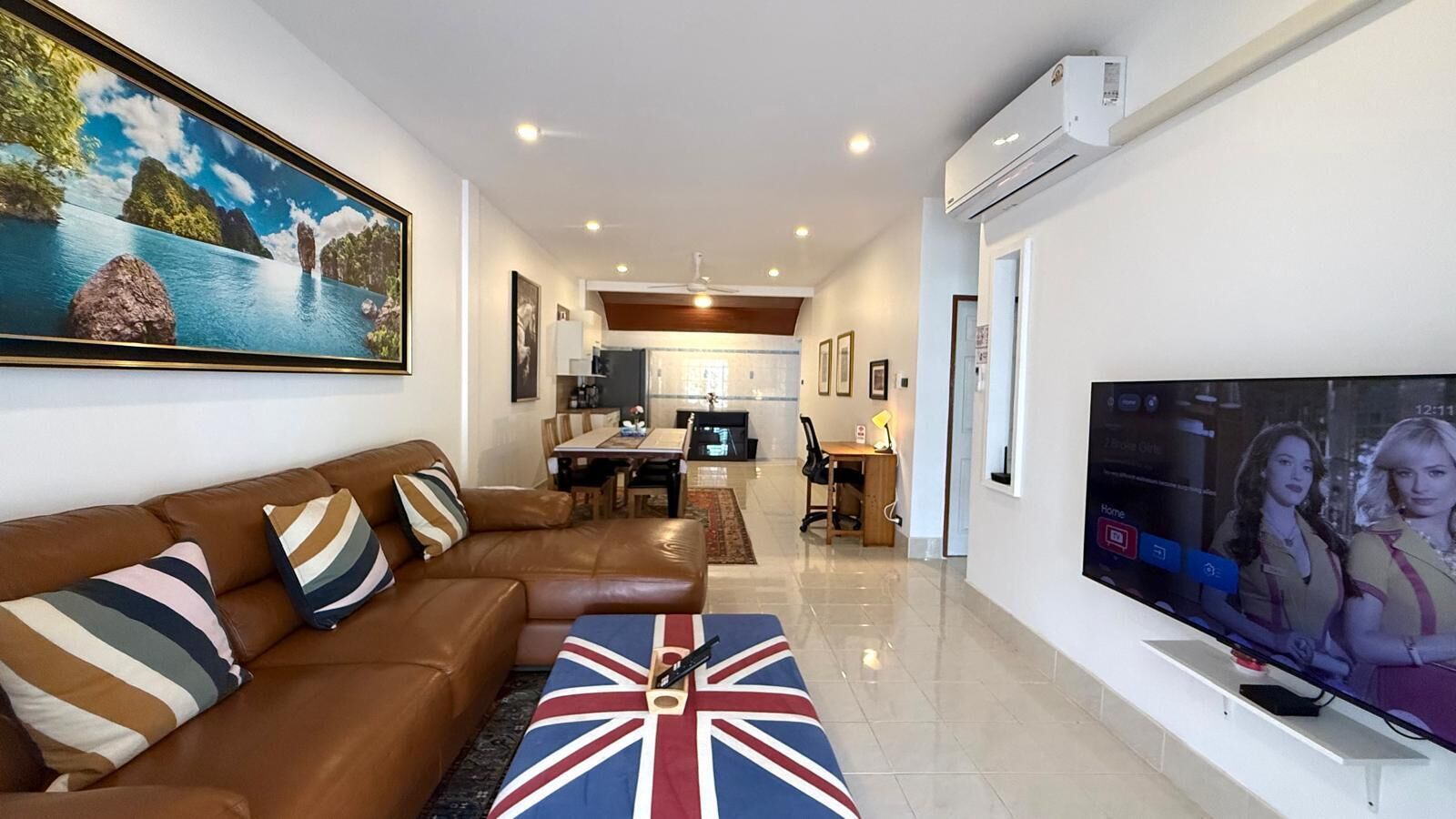 Una sala de estar con un sofá, un televisor y un cuadro. Hay un comedor con una mesa y sillas.