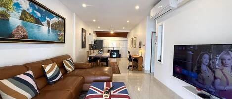 Una sala de estar con un sofá, un televisor y un cuadro. Hay un comedor con una mesa y sillas.