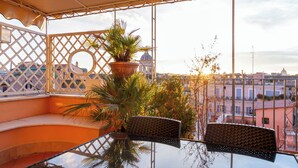 Een balkon met een glazen tafel en stoelen, een bloempot en uitzicht op een stadsgezicht met gebouwen en een koepel.