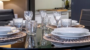 Een eettafel gedekt met helder glaswerk en witte borden, met een keuken op de achtergrond.