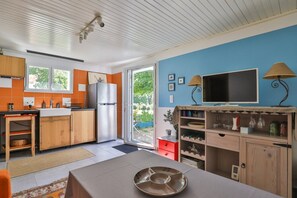 Una cocina moderna con un refrigerador, armarios de madera, una mesa de comedor con un plato y un televisor sobre un soporte.