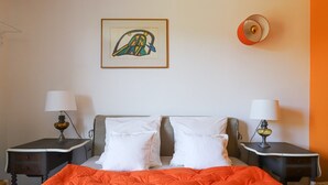Une chambre d’hôtel avec un lit, deux tables de chevet, une lampe fixée au mur et un tableau encadré.