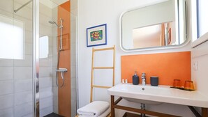 Une salle de bain avec une douche en verre, un lavabo blanc, un porte-serviettes en bois et un miroir.