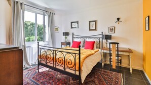 A bedroom with a bed, a nightstand, a desk, and a window with curtains.