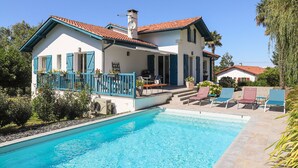 A two-story house with a swimming pool, outdoor furniture, and a garden.