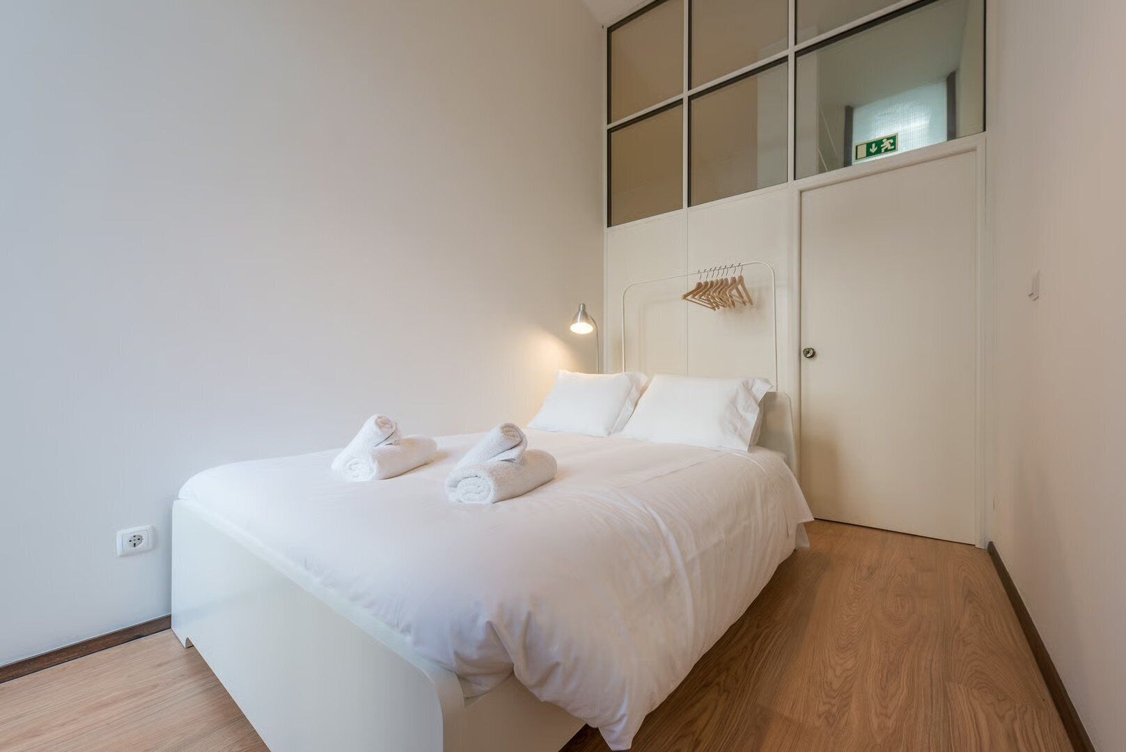 A neatly made bed with white linens and towels, a bedside lamp, and a wooden floor.
