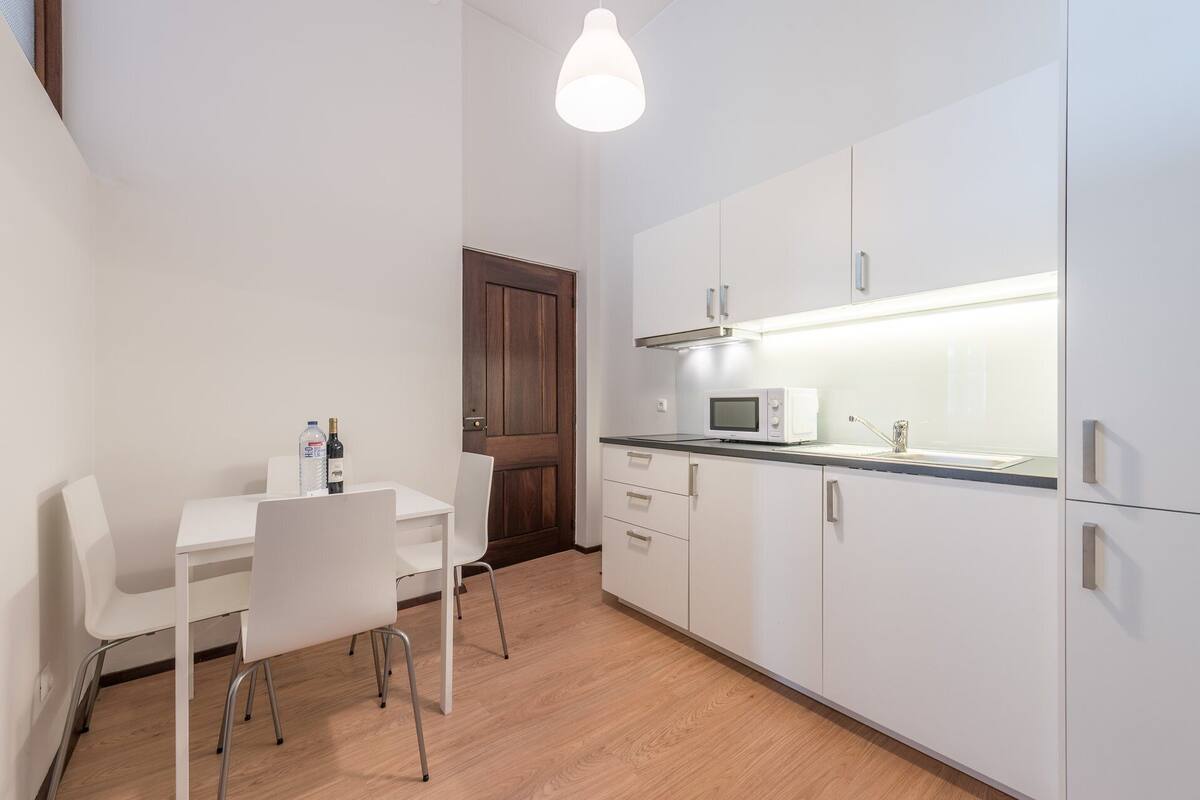 A compact kitchen with white cabinets, a microwave, and a sink under a pendant light.