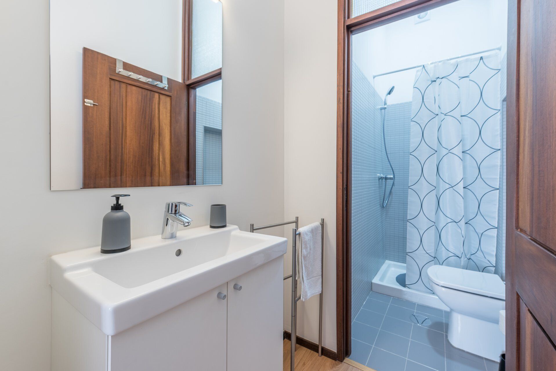 A bathroom with a white sink, a mirror, a towel rack, and a shower with a patterned glass door.
