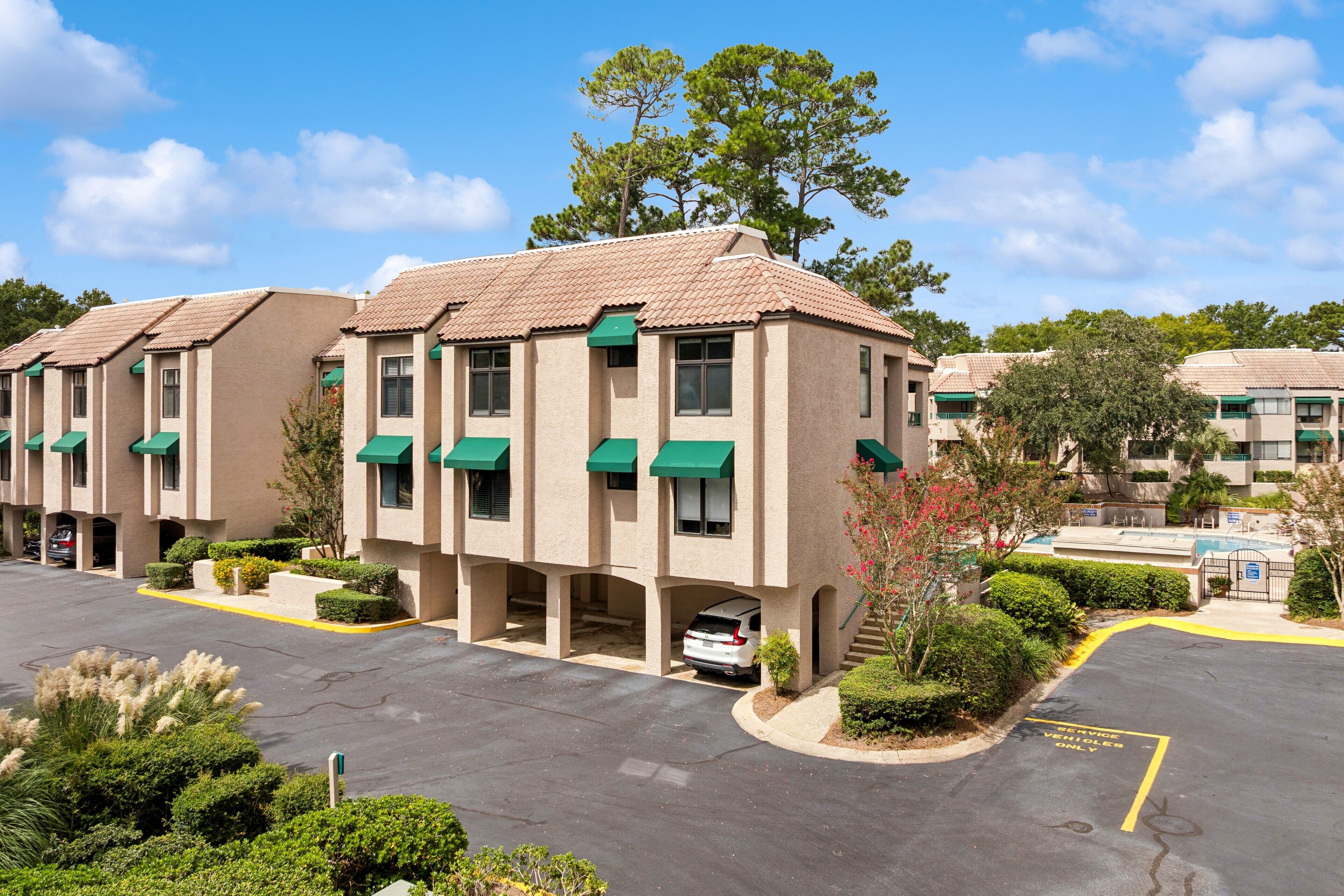 A row of beige buildings with green awnings, a parking lot, and a clear blue sky.