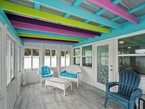 Une véranda avec des poutres au plafond aux couleurs vives, des meubles blancs et de grandes fenêtres.