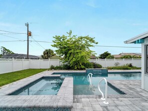 A rectangular pool with two diving boards, surrounded by a white fence and a lush green tree.