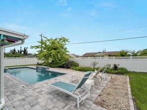 A swimming pool with a small waterfall feature, surrounded by a white fence and lush greenery.
