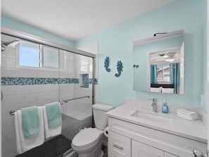 A bathroom with a glass shower enclosure, a toilet, a sink with a mirror above it, and decorative seahorse wall art.