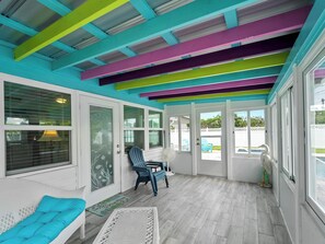 A covered patio area with a colorful ceiling, a white door, and a seating area with a blue chair and a white bench.