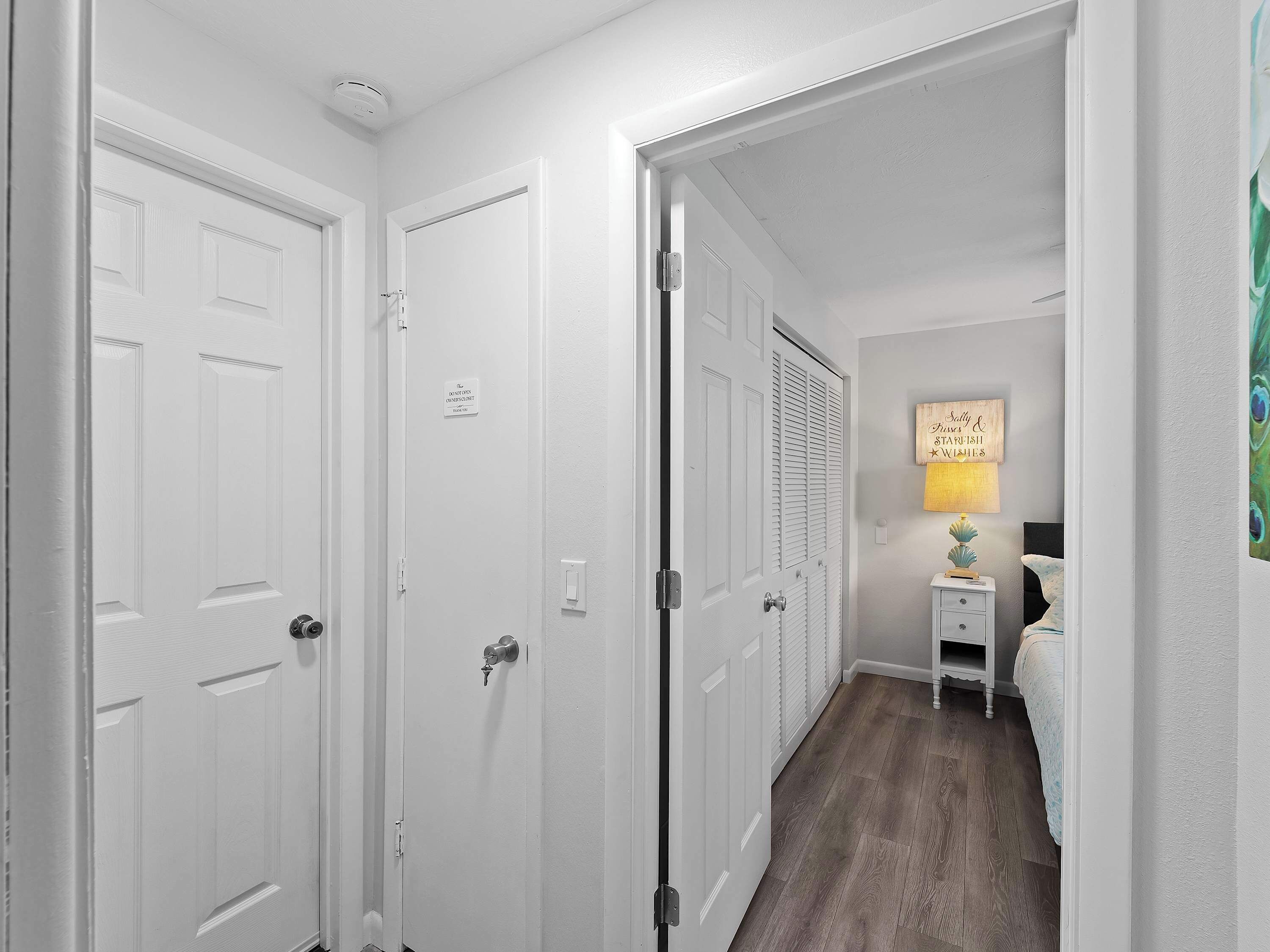 A hallway with white doors, a bedside table with a lamp, and a bed with a blue and white patterned bedspread.