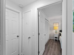 A hallway with white doors, a bedside table with a lamp, and a bed with a blue and white patterned bedspread.