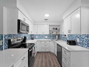 Une cuisine moderne avec des meubles blancs, un four à micro-ondes, un grille-pain et un mixeur.